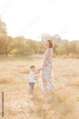 Family with children walking outdoors in summer field at sunset. Pretty mother and her son having fun in summer field. People, family day and lifestyle concept