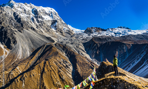 A solo hiker man standing on the ridge at Kyanjin Ri and watching huge snow capped mountains at Langtang National Park in Nepal. Langtang and Kyanjin Ri are popular trekking destinations in Nepal. photo