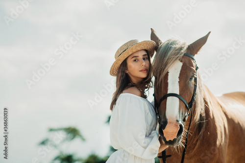 Beautiful hippie girl with horse on a ranch background, front view. The girl in the hat. Soft focus