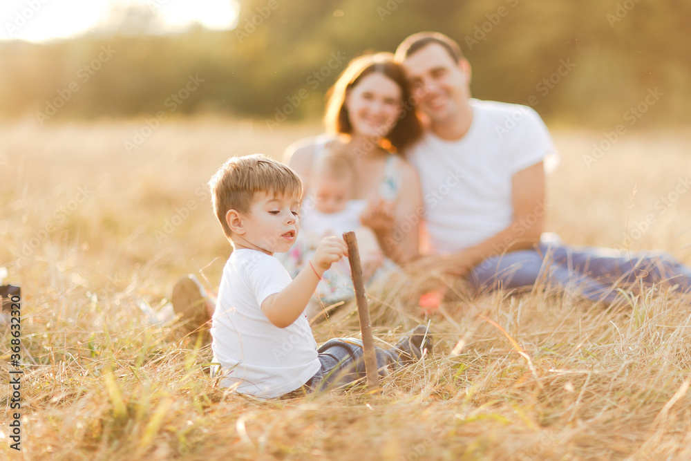Fototapeta premium Family with children walking outdoors in summer field at sunset. Father, mother and two children sons having fun in summer field. People, family day and lifestyle concept