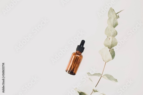 Bottle of aromatic cosmetic or essential oil on a white background surrounded by eucalyptus branches on a white background. Top view. Copy space.