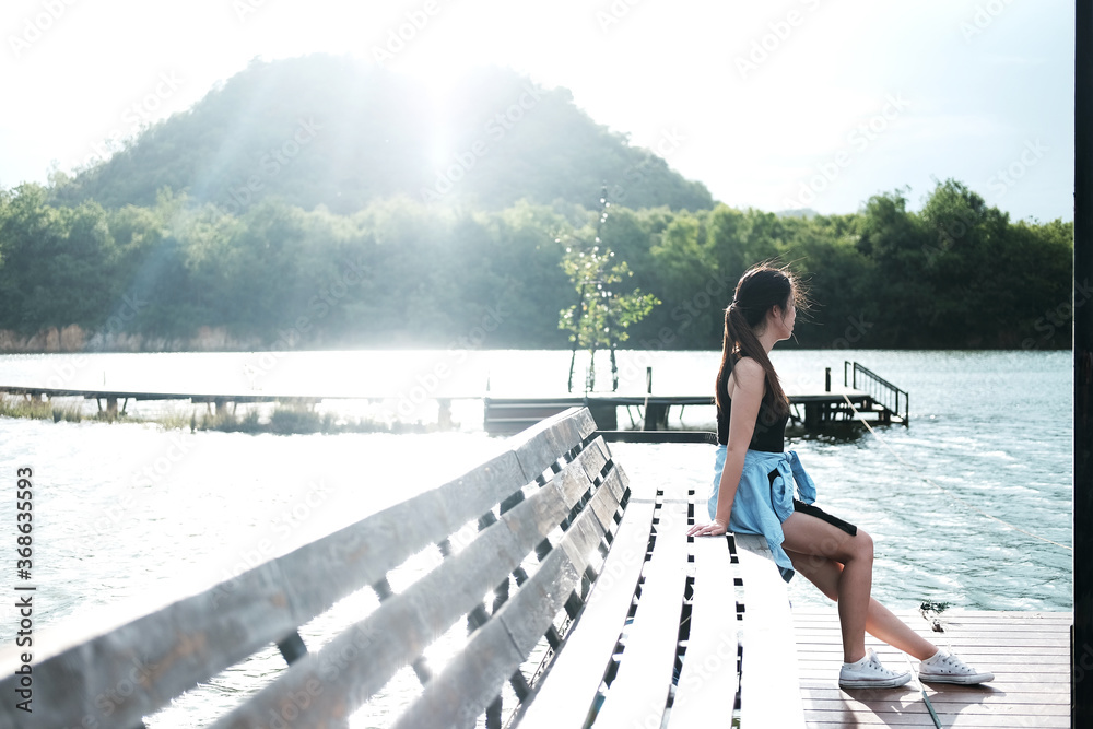 Asian young woman and long hair in black dress stand alone and relaxing on wooden pontoon in river with natural sunlight on summer holiday in the park. Broken heart woman Concept