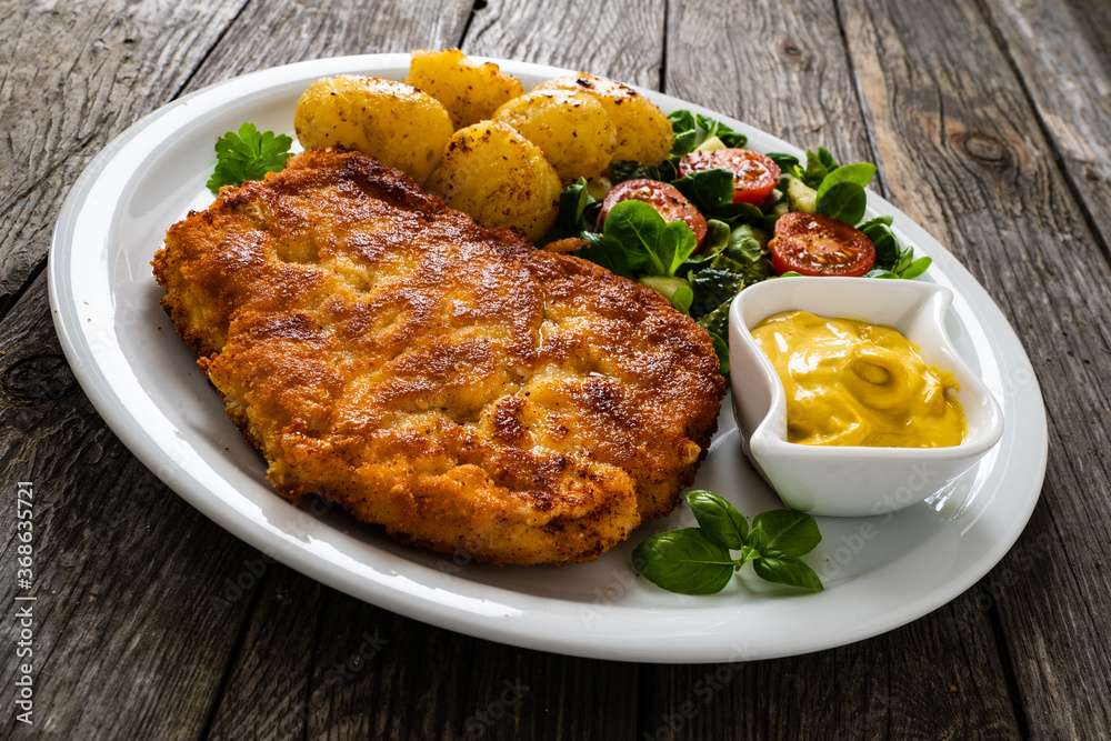 Breaded pork chop with boiled potatoes and vegetable salad on wooden background
Breaded pork chop with boiled potatoes and vegetable salad on wooden background