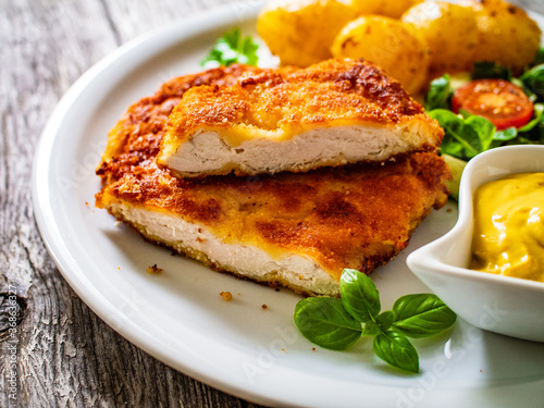 Breaded pork chop with boiled potatoes and vegetable salad on wooden background
