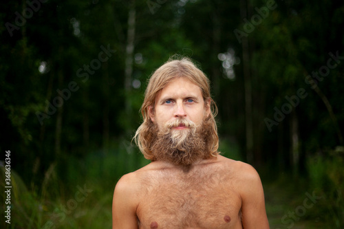A guy with a big beard is resting in the forest. 