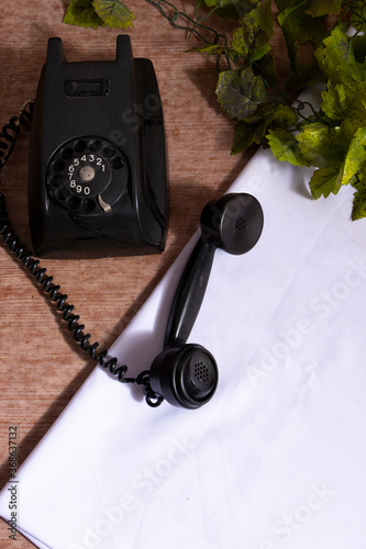 Telefono antiguo sobre mesa de madera con mantel blanco y platas verdes artificiales.  Antigedad negra sobre una mesa photo