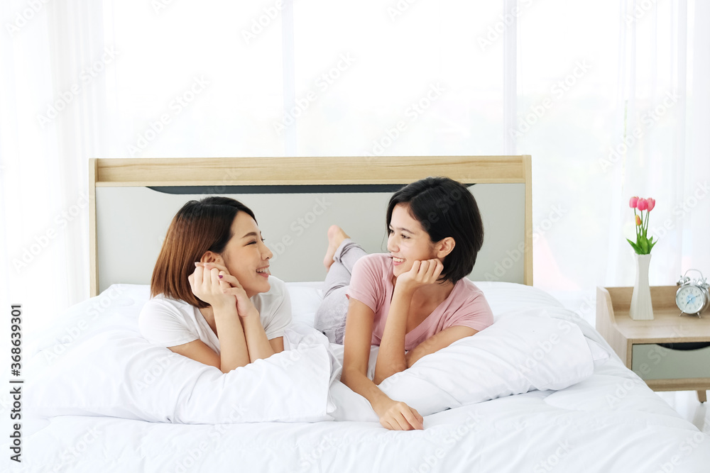 Asian young sisters lovely couple lying on white bed smiling and talking together in bedroom. Homosexual women or Lesbian in love. family and holiday concept. Asian young sisters lovely couple lying on white bed smiling and talking together in bedroom. Homosexual women or Lesbian in love. family and holiday concept.