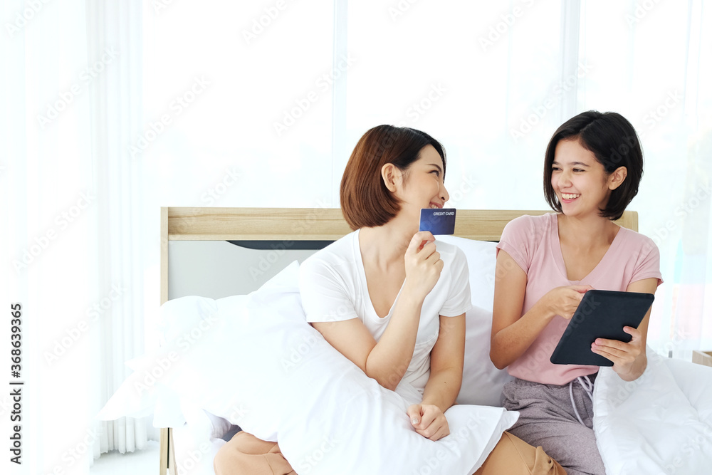 Smiling Asian young sisters lovely couple holding credit card for online shopping in Social website with smartphone and laptop in bedroom together. Smart Technology and homonesexual lesbian Concept Smiling Asian young sisters lovely couple holding credit card for online shopping in Social website with smartphone and laptop in bedroom together. Smart Technology and homonesexual lesbian Concept