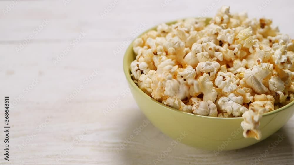 From above crunchy popcorn falling in bowl on white table in slow motion From above crunchy popcorn falling in bowl on white table in slow motion
