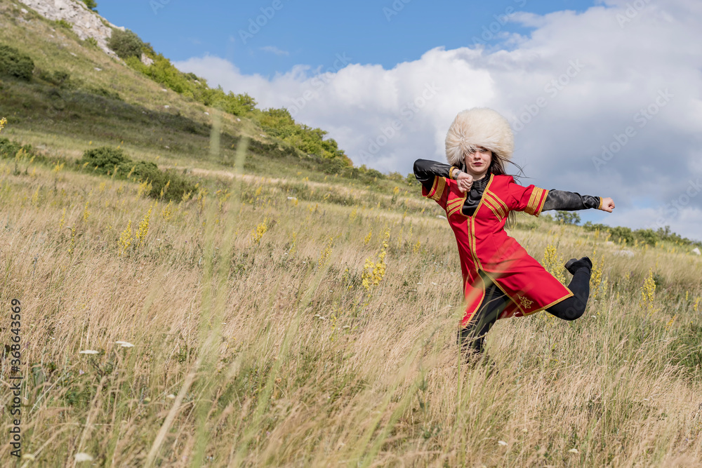A young cheerful girl in a national costume is dancing a fiery dance on a green field at the foot of the mountain A young cheerful girl in a national costume is dancing a fiery dance on a green field at the foot of the mountain
