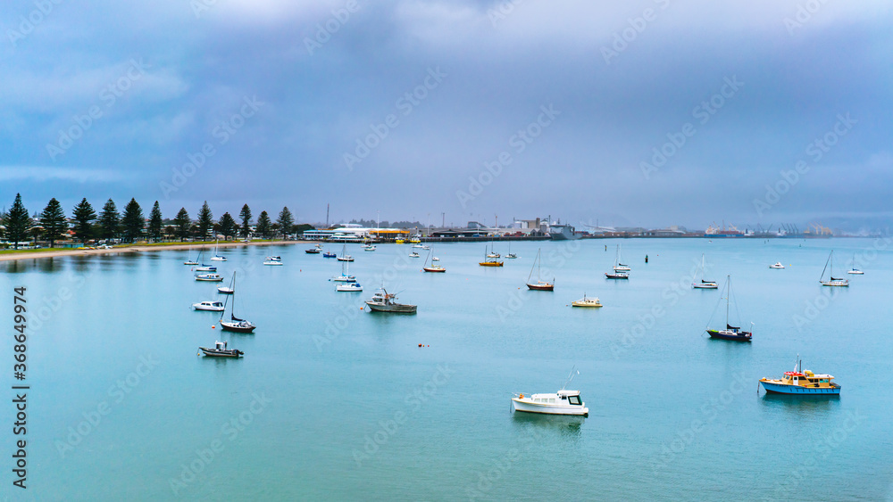 Boats in the harbor on a cloudy day in Tauranga, New Zealand. Pilot Bay Beach in the background.