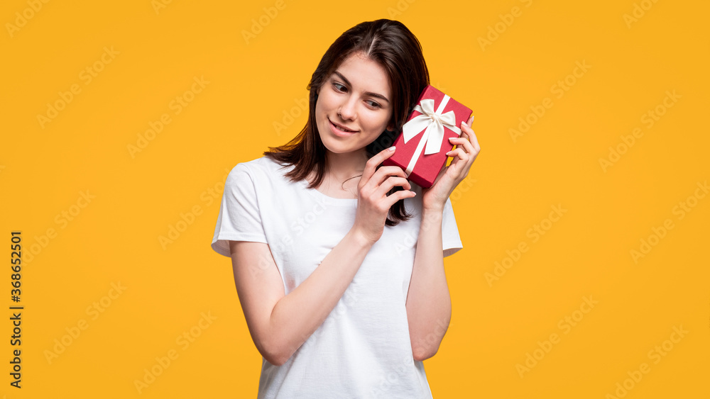 Birthday surprise. Special day. Curious woman in white t-shirt guessing present in gift box isolated on orange copy space. Festive occasion. Holiday congratulation. Birthday surprise. Special day. Curious woman in white t-shirt guessing present in gift box isolated on orange copy space. Festive occasion. Holiday congratulation.