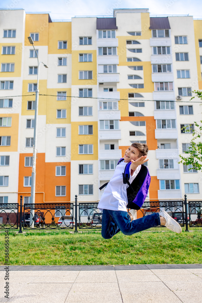 Schoolboy boy jumping high with a school backpack on his back and smiling