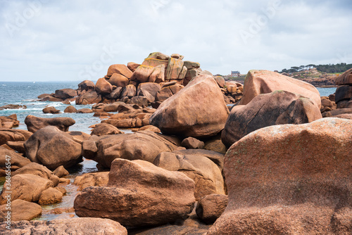 View of unique rock formation at Pink Granite Coast near Tregastel with lonely house at background. Cotes-D'armor, Brittany, France.