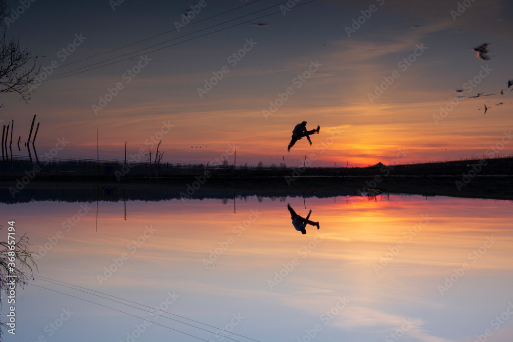 Sunset over the lake and the silhouette of a man with a reflection in the water