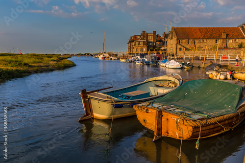 Boats moored on the River Glaven bask in the evening sunset at Blakeney, Norfolk, UK
