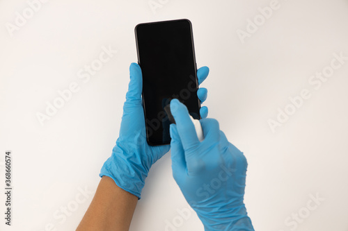 Close up women hands wearing blue protective glove of the hand with a spray of alcohol on the smartphone to clean , Concept of Cleaning dirty screen phone for disease prevention from bacteria. 