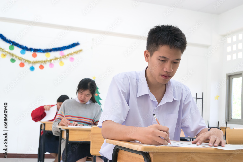 Young Asian students group writing exam on test paper answer sitting on taking final examination in classroom with concentration, Test in high school /university student in exams room Young Asian students group writing exam on test paper answer sitting on taking final examination in classroom with concentration, Test in high school /university student in exams room
