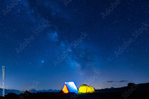Two camping tents glowing under the milky way at night. Camping in the mountains under the starry magical sky. 5 Billion Star Hotel.