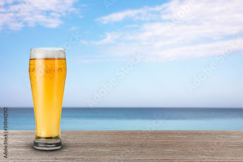 Cold beer on wooden desk against blurred sea. Space for text © New Africa