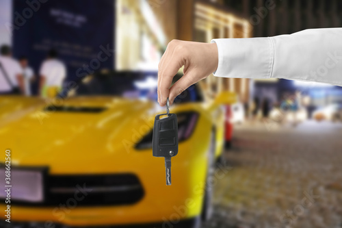 Car buying. Man holding key against blurred automobile, closeup