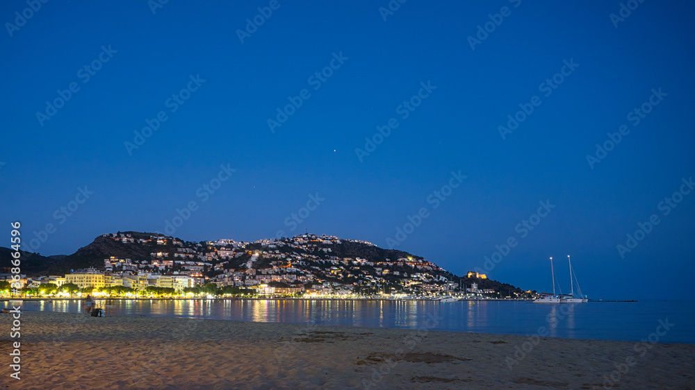 Night view of the small mountain in the bay of Roses full of illuminated houses and the calm sea