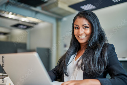 Portrait of smiling young female entrepreneur with long black hair at desk working in creative office