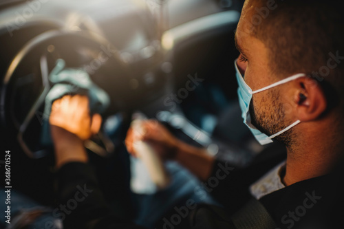 Man with protective face mask cleaning car interior to prevent virus spread 