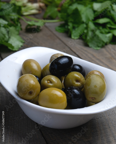 green olives in a bowl. Black and white olives on wood background