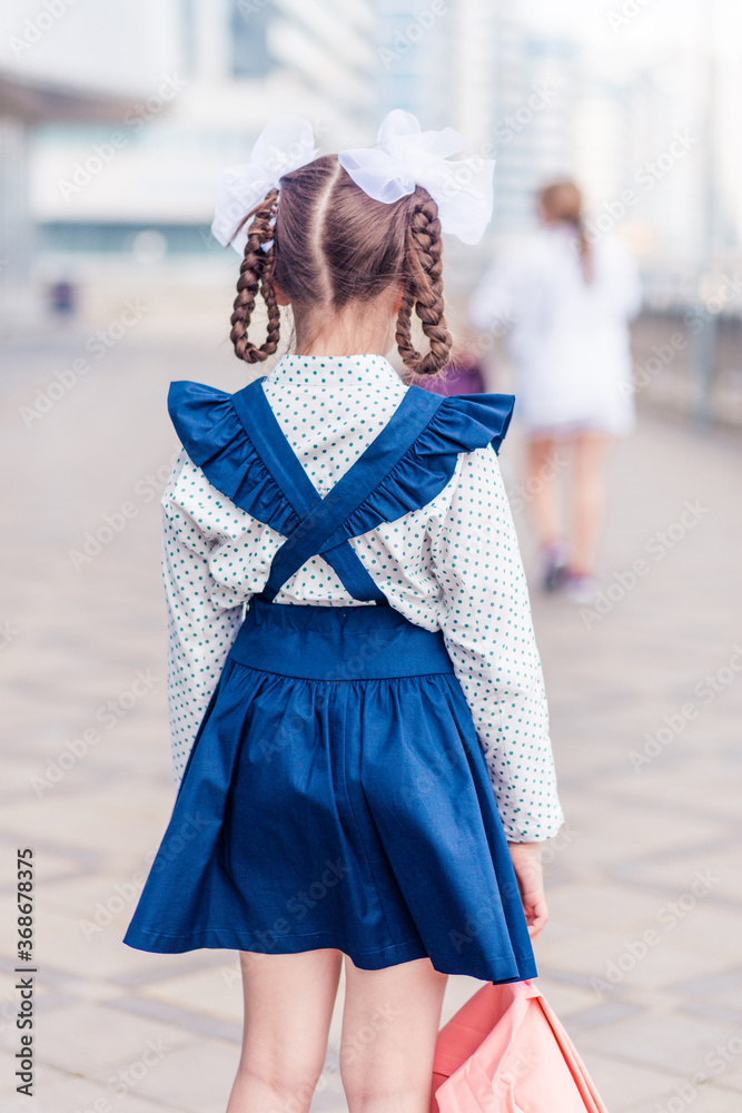 Obraz premium A girl in a school uniform with a backpack on her back stands with her back to the camera