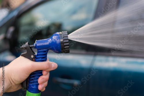 A woman's hand holds a hose for washing the car. Water, spray, jet. The idea is to wash your car in front of your house, saving after a pandemic. Photo close-up, horizontal.