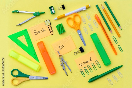 Creative flatlay with stationery on the bright yellow background with "Back to school" phrase written on sticker surrounded by school supplies 