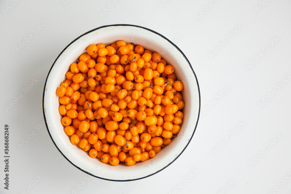 Handful of useful medicinal sea buckthorn berries in a white bowl on a white isolated background. Handful of useful medicinal sea buckthorn berries in a white bowl on a white isolated background.