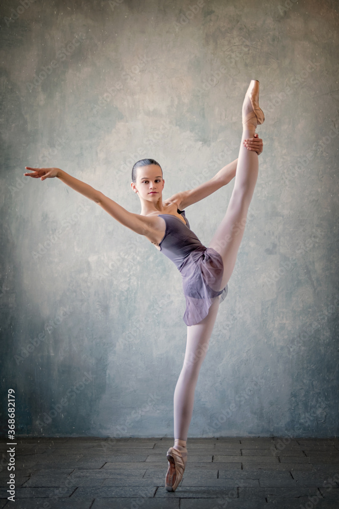 graceful ballet dancer in a light lilac suit and pointe shoes against a gray wall. Dance, grace, artist, contemporary, movement, action and freedom of movement concept.