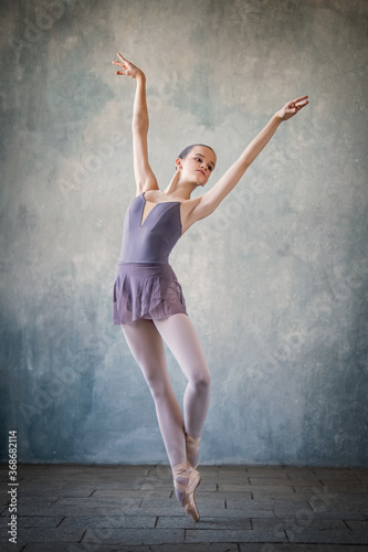 graceful ballet dancer in a light lilac suit and pointe shoes against a gray wall. Dance, grace, artist, contemporary, movement, action and freedom of movement concept.