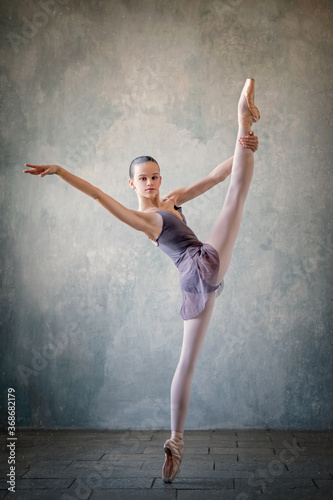 graceful ballet dancer in a light lilac suit and pointe shoes against a gray wall. Dance, grace, artist, contemporary, movement, action and freedom of movement concept. © Maria Moroz