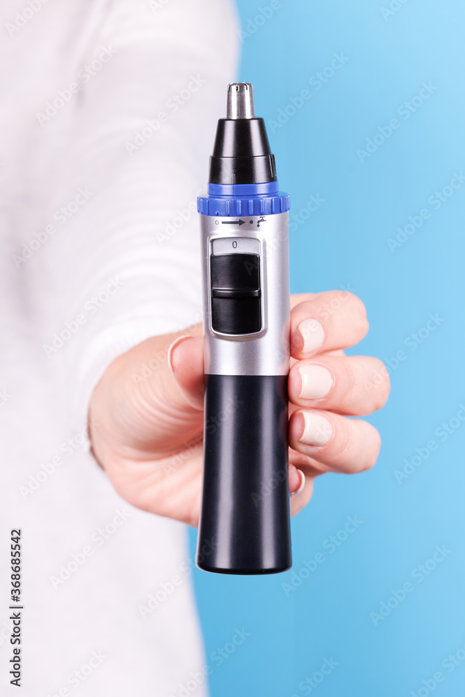 Hand with nose trimmer, hair electric cutter. Isolated on blue background. Hand with nose trimmer, hair electric cutter. Isolated on blue background.