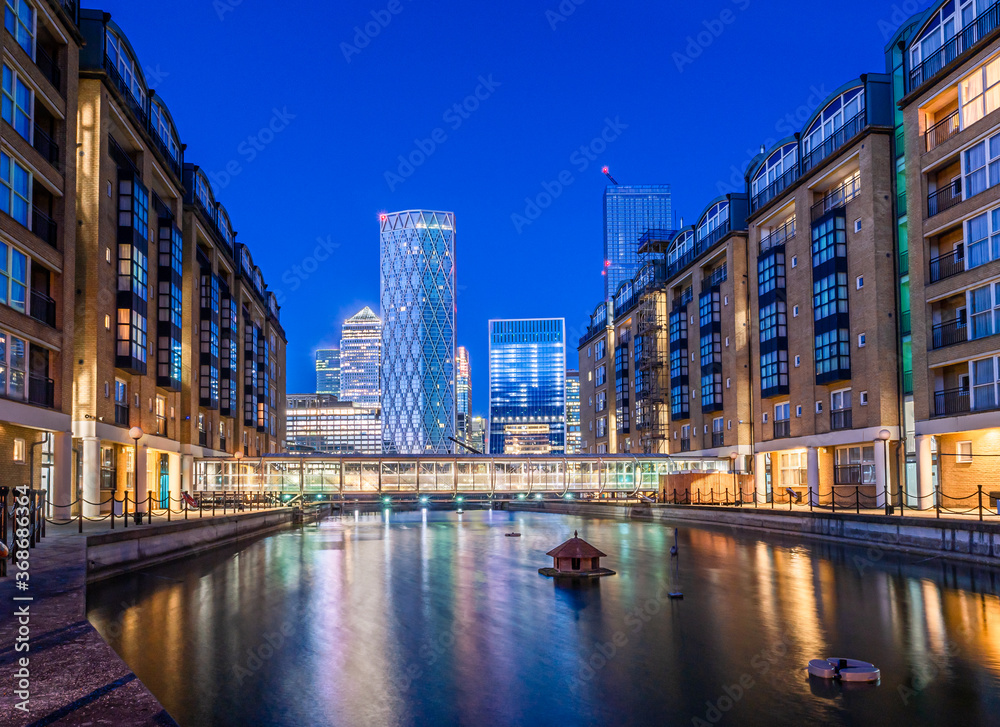 Night scene of the Canary Wharf financial buildings and residential houses reflected in the river Thames