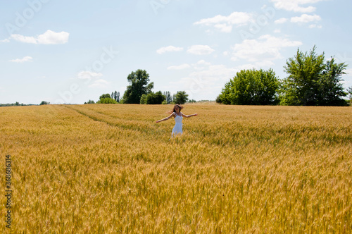optimistic female smiling in wheat field. stylish young woman. girl with windy hair. Young caucasian woman joyful and carefree. woman wearing white casual dress. dance in summer field. she is happy © altana_studio