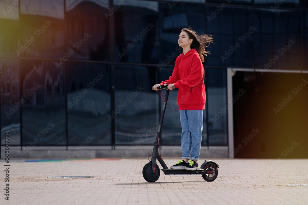 Φωτογραφία Cute teenager girl riding electric kick scooter in a cityscape