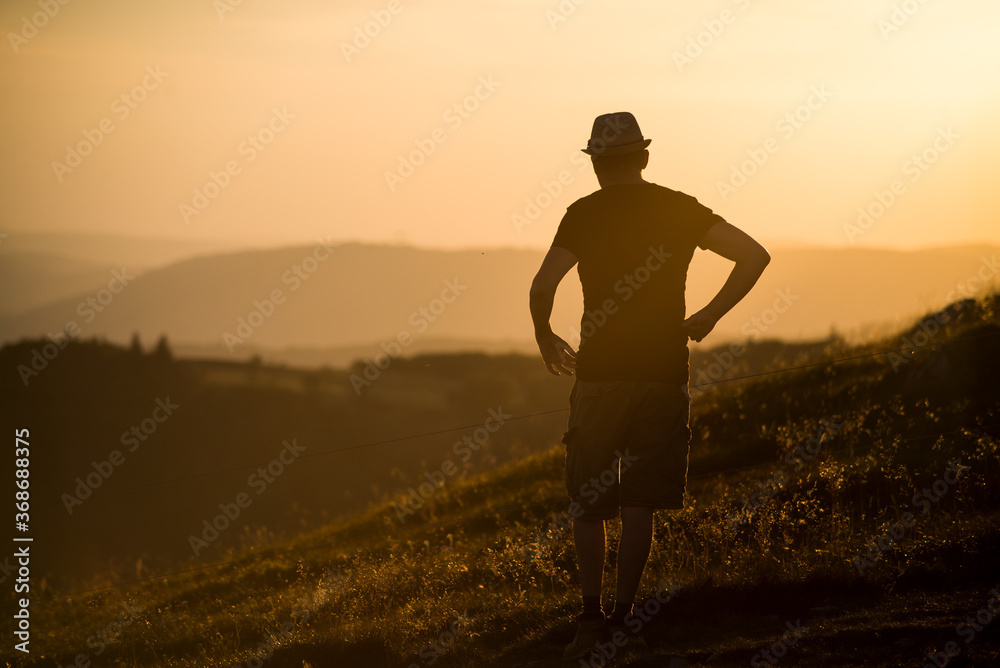 Portrait  of man silhouette standing at the top of the mountain looking the lanscape on sunset background