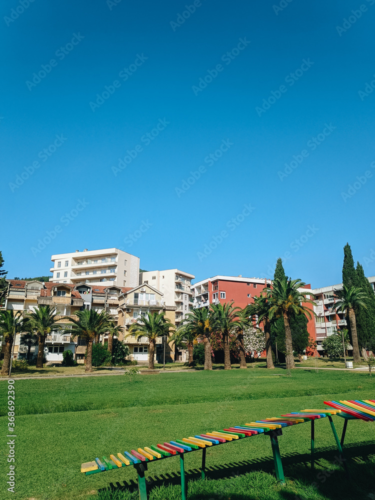 Yugoslavian houses in the center of Budva in Montenegro, next to the city park and green date palms, with a green lawn and blue skies in summer.