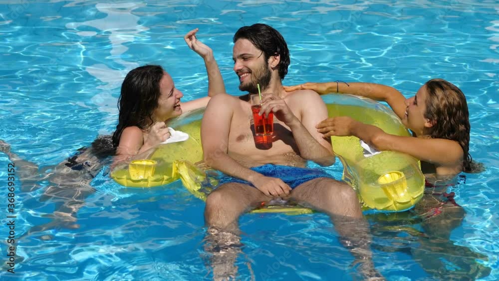 young man relaxing on the inflatable in the pool with his friends caressing him young man relaxing on the inflatable in the pool with his friends caressing him