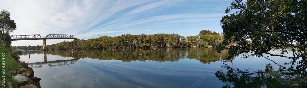 Beautiful panoramic view of a river with reflections of tall pedestrian bridge, trees and blue sky, Parramatta river, Rydalmere, New South Wales, Australia Beautiful panoramic view of a river with reflections of tall pedestrian bridge, trees and blue sky, Parramatta river, Rydalmere, New South Wales, Australia