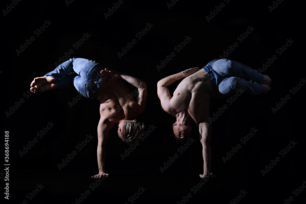 two twin brothers in blue jeans with a naked torso perform acrobatic elements, black background