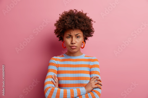 Insulted dark skinned woman stands wih arms folded over body, looks from under forehead with frowned eyebrows, feels angry and displeased, waits for apology. You promised to buy this for me.