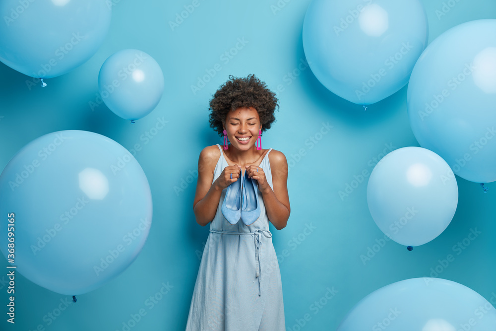Fototapeta premium I want to wear this high heeled blue shoes. Happy woman chooses best outfit of favorite color from wardrobe, tries new dress and footwear, satisfied after visiting luxury boutique. Women fashion