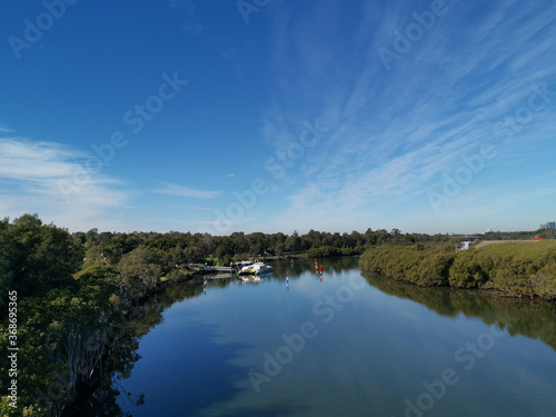 Beautiful view of a river and a wharf with reflections of blue sky, light clouds and trees on water, Parramatta river, Rydalmere, New South Wales, Australia