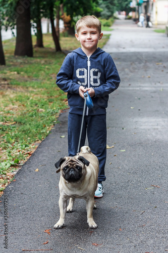 Happy boy walks on the street of the city with a small dog. Autumn family walk with a pug. Safe walk in the street, away from strangers. Family pet.