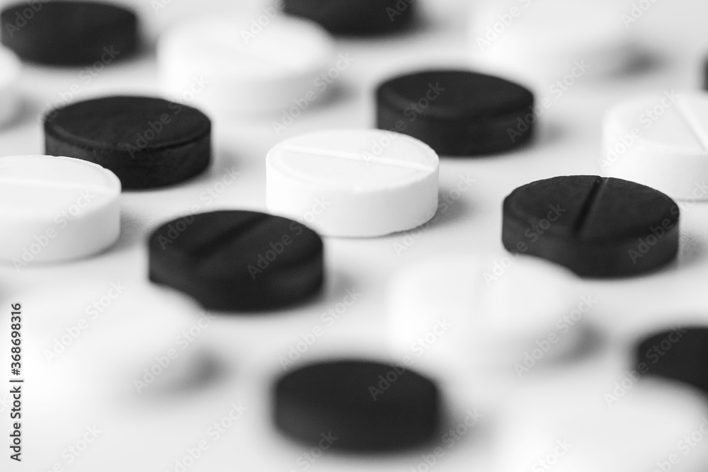 Close up of black and white pills lie exactly in a row on a white table. Isolated pharmaceutical drug background Close up of black and white pills lie exactly in a row on a white table. Isolated pharmaceutical drug background